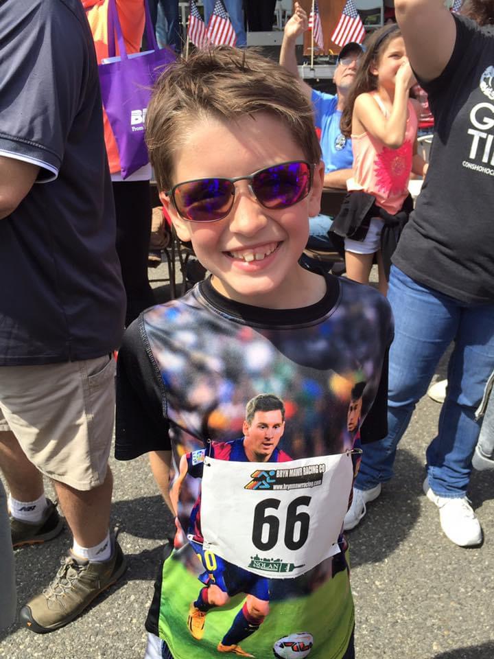 Parker as a young boy at a local fun-run, race bib number 66, smiling in sunglasses