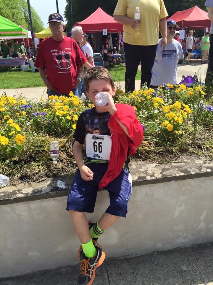 Parker as a young boy taking a drink from a water bottle after a fun-run, race bib 66